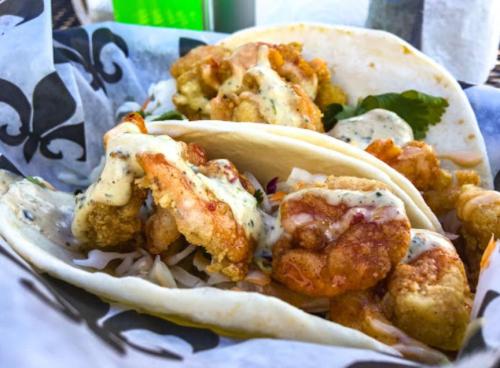 Three shrimp tacos filled with crispy shrimp, slaw, and drizzled with a creamy sauce, served in soft tortillas.