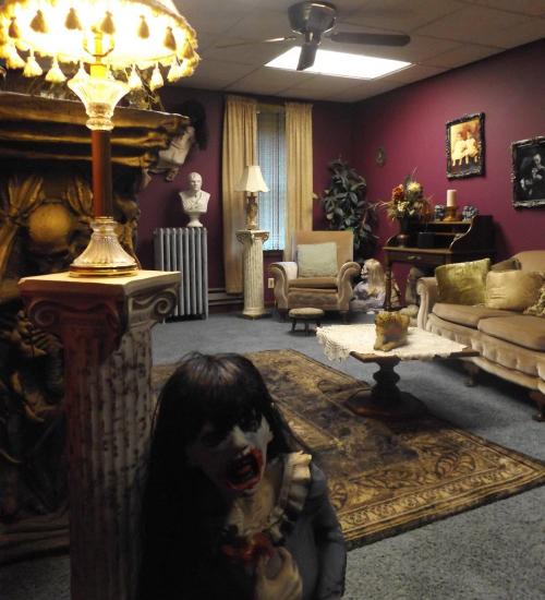 A dimly lit room with dark red walls, featuring vintage furniture and a creepy doll in the foreground.