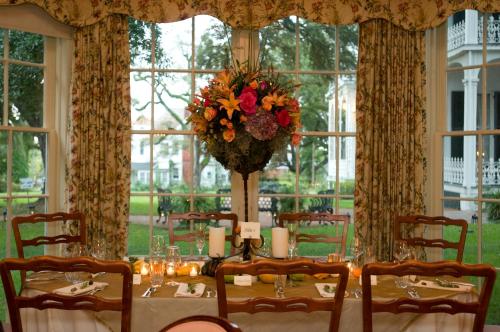 A beautifully set dining table with floral centerpiece, candles, and large windows overlooking a garden.