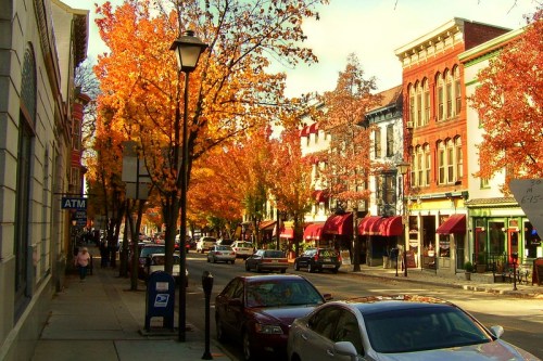 A charming street lined with colorful autumn trees and historic buildings, with cars parked along the curb.