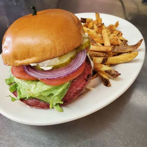 A juicy burger with lettuce, tomato, pickles, and onion, served with a side of crispy fries on a white plate.