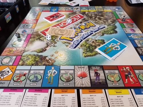 A Pokémon-themed Monopoly game board with cards, dice, and player pieces on a table.