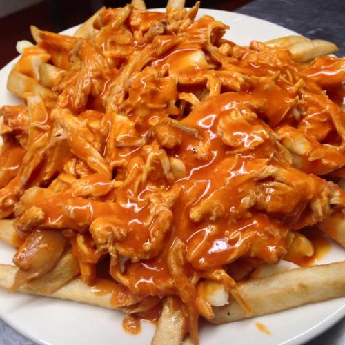 A plate of French fries topped with shredded chicken and a rich orange sauce.