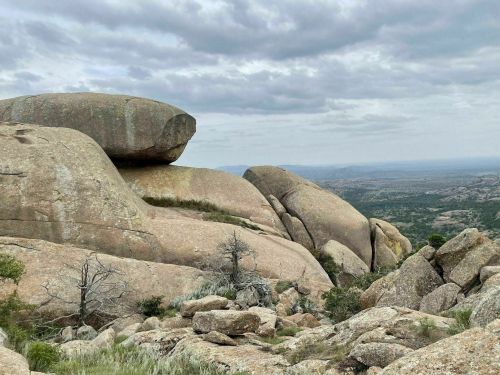 A rocky landscape with large boulders and a cloudy sky, showcasing rugged terrain and distant hills.