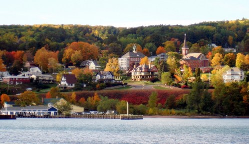 A scenic view of a lakeside town in autumn, featuring colorful trees and charming buildings against a clear sky.
