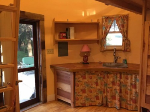 Cozy kitchen with wooden countertops, a sink, and colorful curtains, featuring a door leading outside.