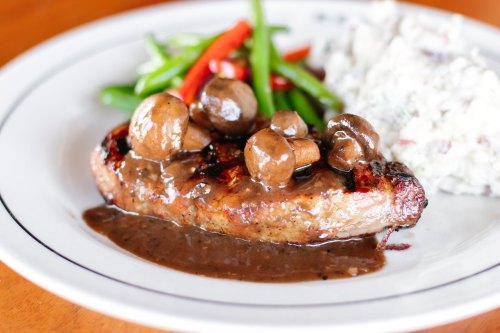 A plate featuring grilled steak topped with mushroom sauce, served with green beans and a side of creamy coleslaw.