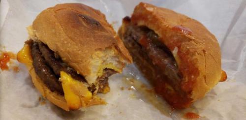 A split hamburger with melted cheese and sauce, resting on white paper.