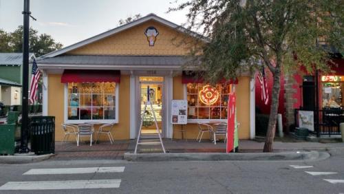 A colorful ice cream shop with outdoor seating, flags, and festive lights, located on a street corner.