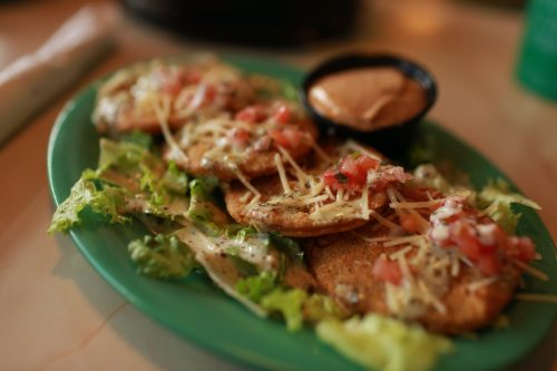 A plate of crispy tortillas topped with cheese, tomatoes, and lettuce, served with a side of dipping sauce.