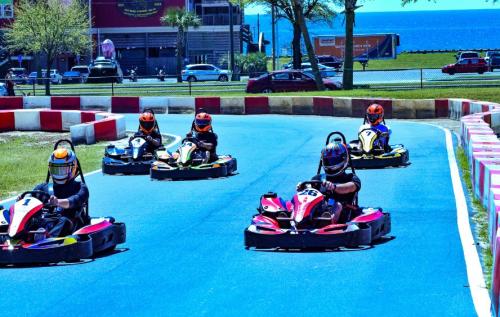 A group of go-kart racers compete on a track with a scenic view of the ocean in the background.