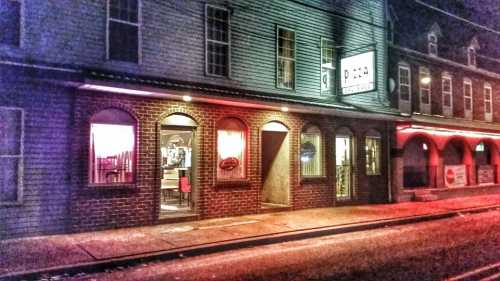 A brick building at night with illuminated windows, featuring a pizza restaurant sign and colorful lighting.