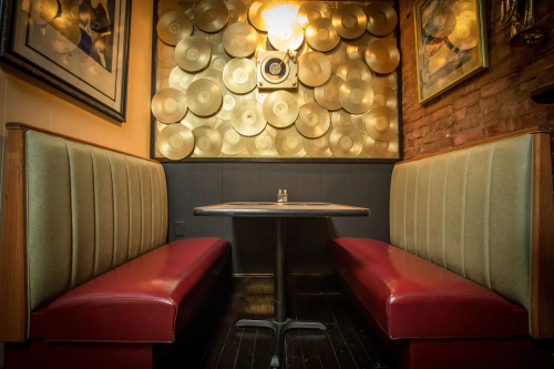 Cozy restaurant booth with red seating and a wall adorned with gold records. Warm lighting creates an inviting atmosphere.
