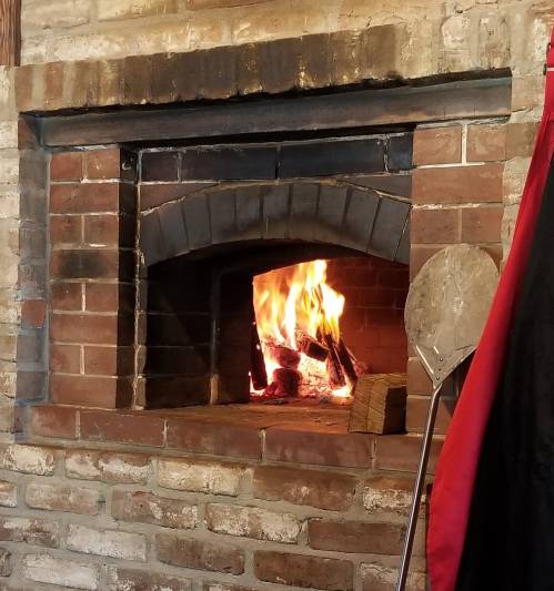 A cozy brick fireplace with a roaring fire and a pizza peel resting nearby.