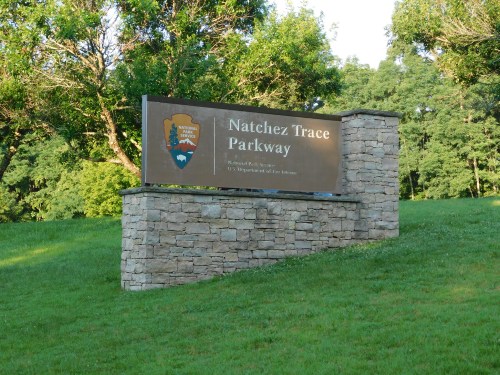 Sign for Natchez Trace Parkway, featuring a stone base and surrounded by green grass and trees.
