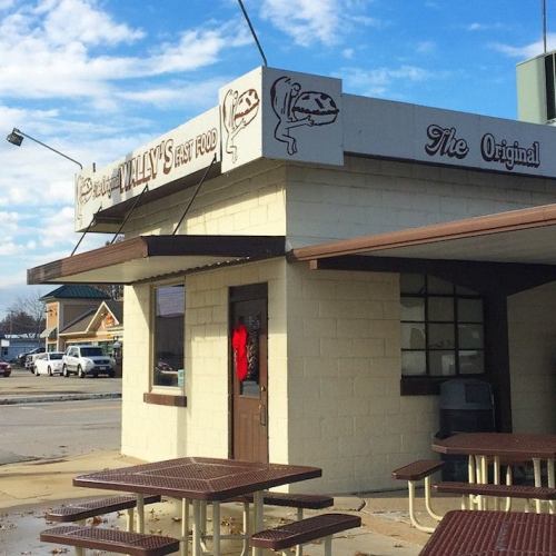 A small fast food restaurant named "Wally's" with outdoor seating and a cloudy sky in the background.