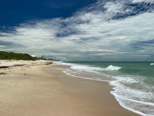 A serene beach scene with gentle waves, soft sand, and a cloudy sky in the background.