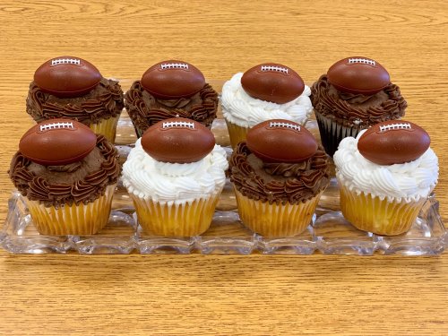 A tray of nine cupcakes, half with chocolate frosting and half with white frosting, each topped with a chocolate football.