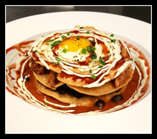 A plate of stacked tortillas topped with pulled meat, a fried egg, sauce, and drizzled with cream and green onions.