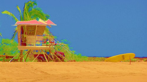 A colorful lifeguard tower on a sandy beach with a surfboard nearby and palm trees in the background.