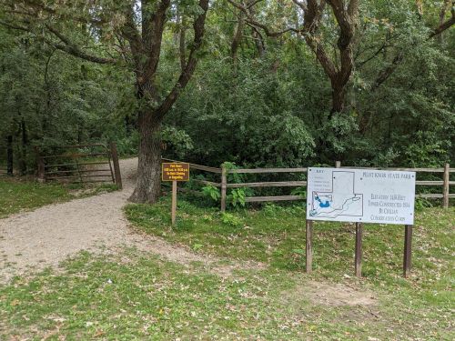 Entrance to Pilot Knob State Park, featuring a trail map and a sign about park rules, surrounded by trees.