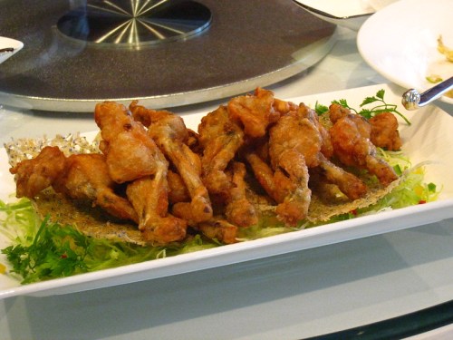 A platter of crispy fried chicken wings garnished with lettuce and herbs, served on a white dish.