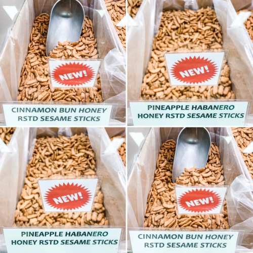 Four containers of flavored sesame sticks: Pineapple Habanero and Cinnamon Bun Honey, with a scoop in each.