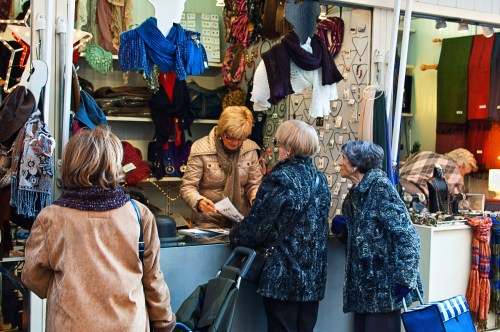 A market stall with colorful scarves and accessories, where three women are interacting with a vendor.