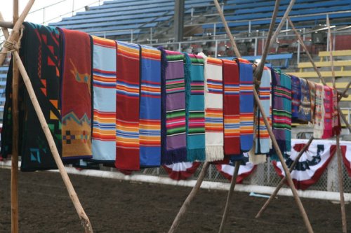 Colorful woven blankets hang on a display, showcasing various patterns and designs at an outdoor event.