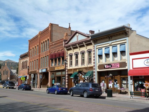 Historic buildings line a street, featuring shops and restaurants under a clear blue sky.