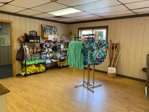 A cozy shop interior featuring clothing racks, shelves of merchandise, and wooden flooring.