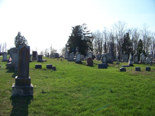 A peaceful cemetery with various gravestones set on a grassy hillside under a clear sky.