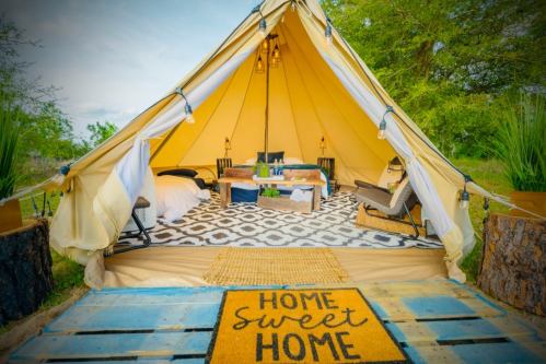 A cozy glamping tent with a welcome mat, stylish decor, and comfortable seating in a natural outdoor setting.