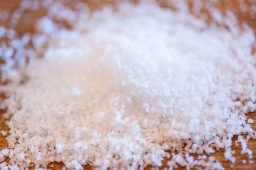 A close-up of a pile of coarse white salt on a wooden surface.