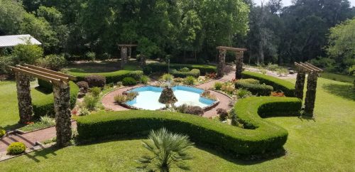 Aerial view of a landscaped garden featuring a circular pool, stone pathways, and lush greenery.