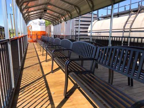 A row of black benches under a covered walkway, with a train car visible in the background.