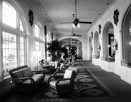 A spacious, elegant hallway with arched windows, ceiling fans, and comfortable seating in a black and white setting.