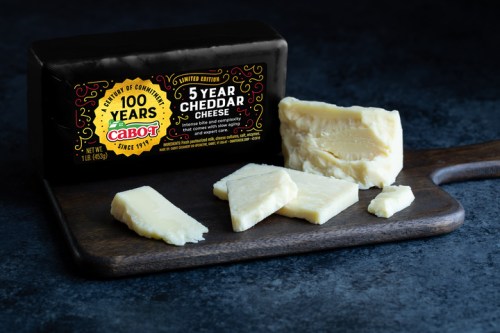 A block of Cabot 5 Year Cheddar Cheese on a wooden board, with several slices cut and displayed beside it.