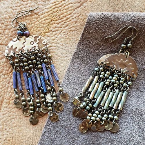 Two ornate earrings with metal and bead designs, featuring dangling elements in blue and silver tones on a textured background.