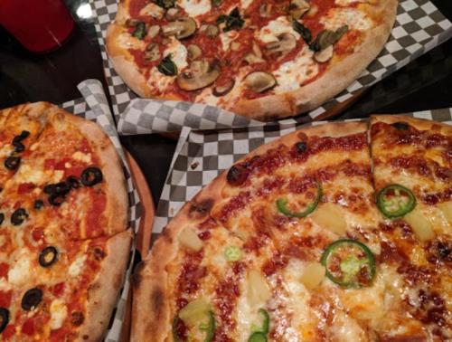 Three pizzas on checkered paper: one with olives, one with mushrooms, and one topped with jalapeños and pineapple.