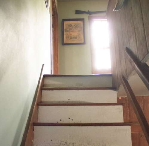 A staircase leading up to a window, with a framed picture on the wall and wooden railing.