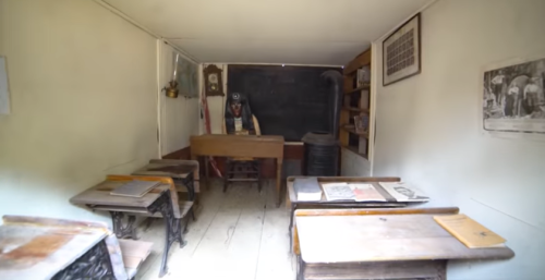 A vintage classroom with wooden desks, a teacher's desk, and a blackboard, evoking a historical educational setting.