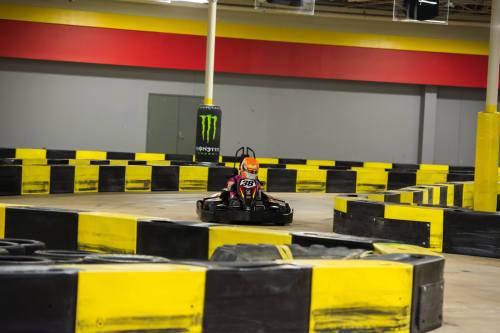 A go-kart racing on a winding track with yellow and black barriers in an indoor facility.