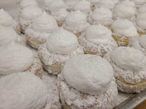 A close-up of fluffy pastries topped with whipped cream and dusted with powdered sugar, arranged on a tray.