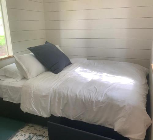 Cozy bedroom with a single bed, white bedding, and a large gray pillow against a light wooden wall.