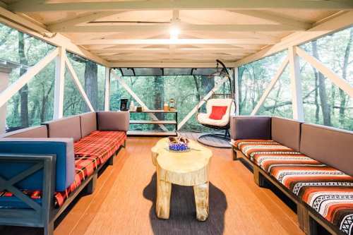 Cozy outdoor seating area with a wooden table, surrounded by trees, featuring a hanging chair and plaid blankets.