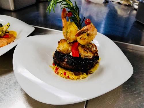 A gourmet dish featuring a blackened patty topped with shrimp, garnished with rosemary, served on a bed of rice.
