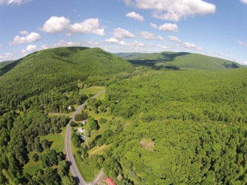 Aerial view of lush green mountains and a winding road surrounded by dense forest under a clear blue sky.
