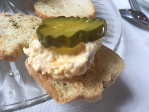 A slice of toasted bread topped with creamy spread and a slice of pickle.