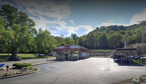A retro-style diner with a colorful sign, surrounded by trees and a parking lot on a sunny day.
